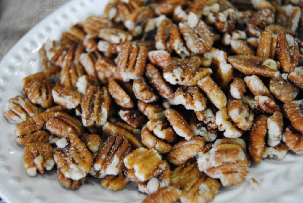 close up of roasted and salted pecans on a white plate